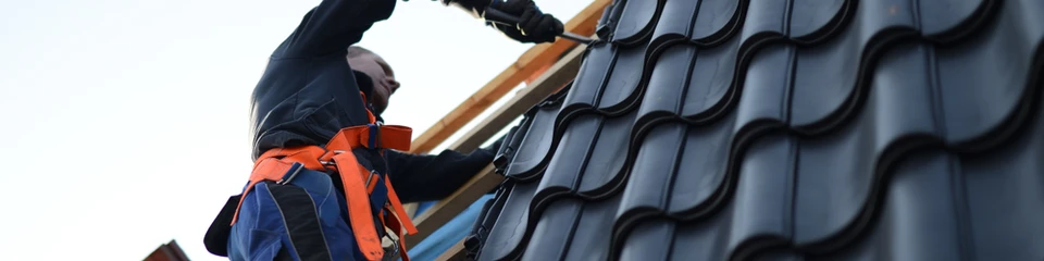 Ouvrier couvreur en tenue de s&eacute;curit&eacute; orange et bleue travaillant sur une toiture en pente