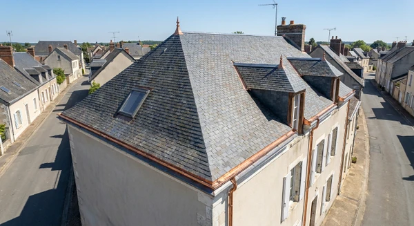 Photographie a&eacute;rienne ou vue en l&eacute;g&egrave;re plong&eacute;e d'une maison ancienne typique de Nogent-le-Rotrou, avec toiture en ardoises grises ou tuiles, situ&eacute;e dans un contexte urbain ou p&eacute;ri-urbain de province. La maison doit pr&eacute;senter clairement ses &eacute;l&eacute;ments de toiture&nbsp;: goutti&egrave;res m&eacute;talliques visibles, solins, ch&eacute;neaux. Environnement architectural et paysager caract&eacute;ristique de la r&eacute;gion Perche. Jour ensoleill&eacute;, ciel d&eacute;gag&eacute;. Aucune personne visible. Composition nette et professionnelle mettant en avant la structure du toit et les d&eacute;tails de zinguerie, distincte des maisons rurales isol&eacute;es d&eacute;j&agrave; s&eacute;lectionn&eacute;es.