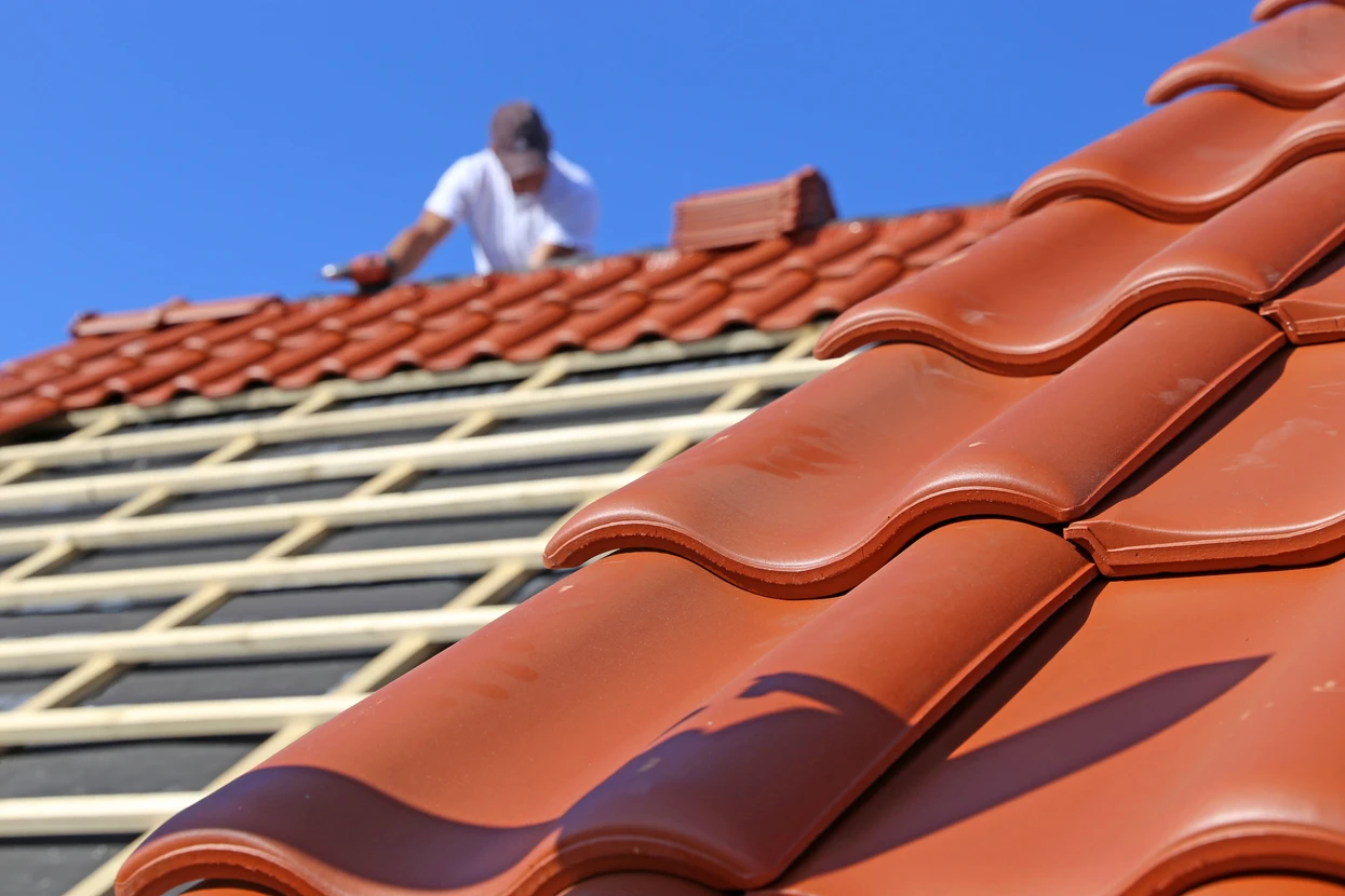 Ouvrier couvreur installant des tuiles terre cuite sur toiture en construction, ciel bleu dégagé, chantier de rénovation