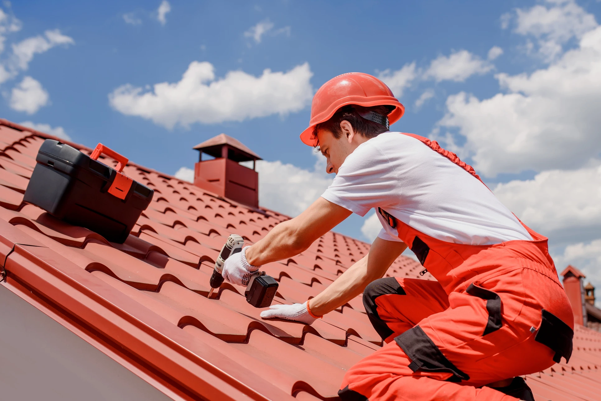 Ouvrier en combinaison rouge et casque de sécurité effectuant des travaux de maintenance sur toiture en tuiles terre cuite