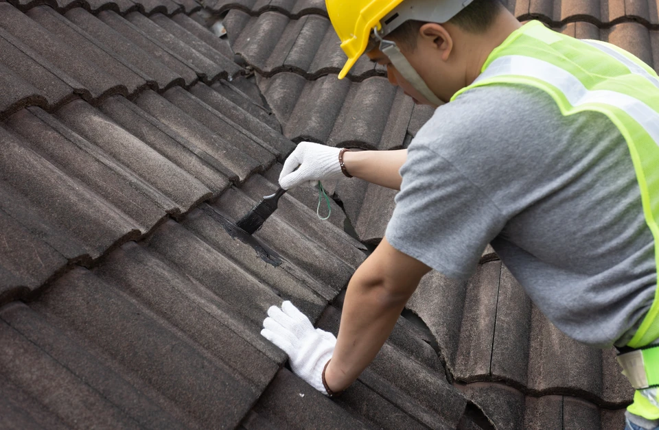 Un ouvrier du b&acirc;timent inspecte les tuiles de toit fissur&eacute;es