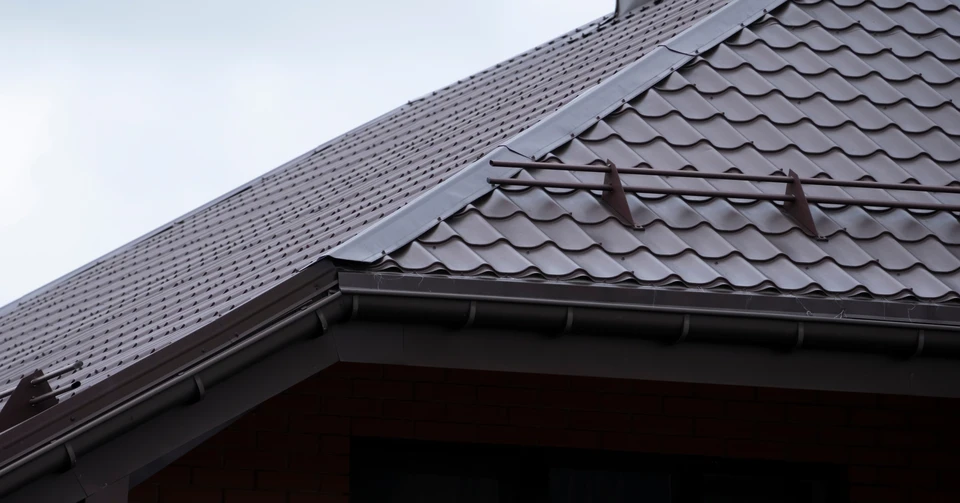 Ouvrier en tenue de protection bleue et casque blanc travaillant sur une toiture en tuiles grises
