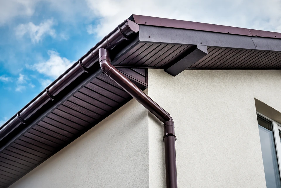 Installateur posant une gouttière blanche en PVC sur bordure de toit avec mur en briques oranges